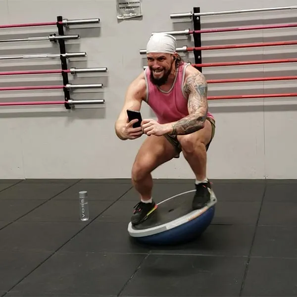Josh squatting on a BOSU ball in the gym, filming on his phone